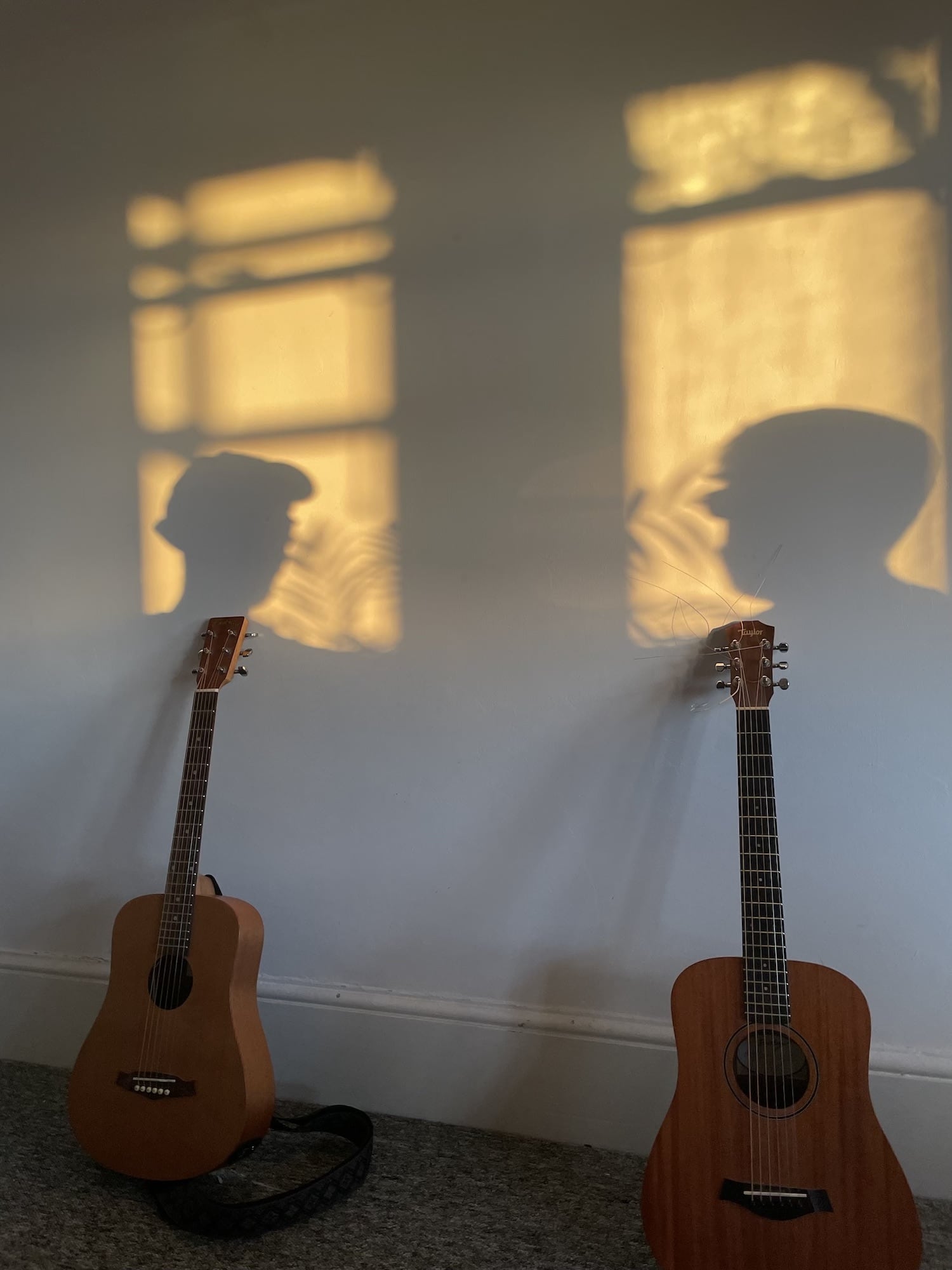 Two travel acoustic guitars leaning against a wall with shadows